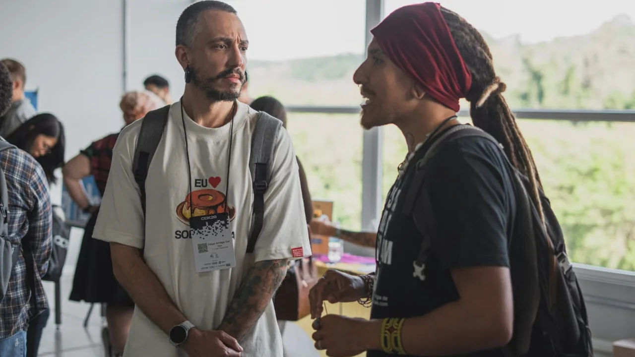 Duas pessoas conversando de perfil num corredor, uma gesticulando.